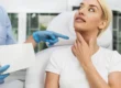 Blonde woman touches her neck as a person in scrubs points during a Speech & Swallowing Disorders consultation in North Logan, UT.