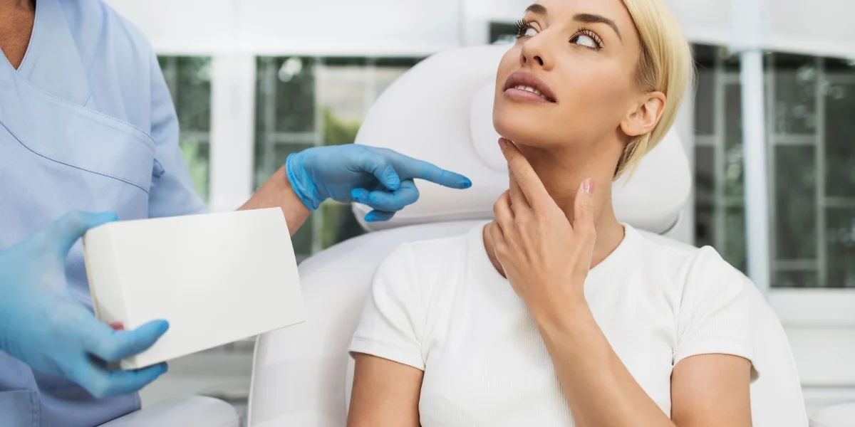 Blonde woman touches her neck as a person in scrubs points during a Speech & Swallowing Disorders consultation in North Logan, UT.
