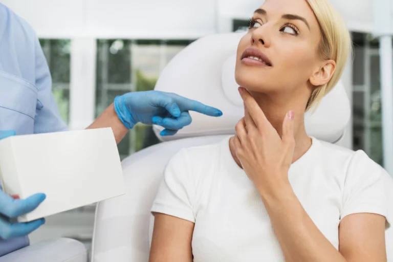 Blonde woman touches her neck as a person in scrubs points during a Speech & Swallowing Disorders consultation in North Logan, UT.