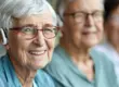 Close-up of a smiling senior woman with white hair, red glasses, and a hearing aid during a Hearing Loss consultation in North Logan, UT