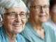Close-up of a smiling senior woman with white hair, red glasses, and a hearing aid during a Hearing Loss consultation in North Logan, UT